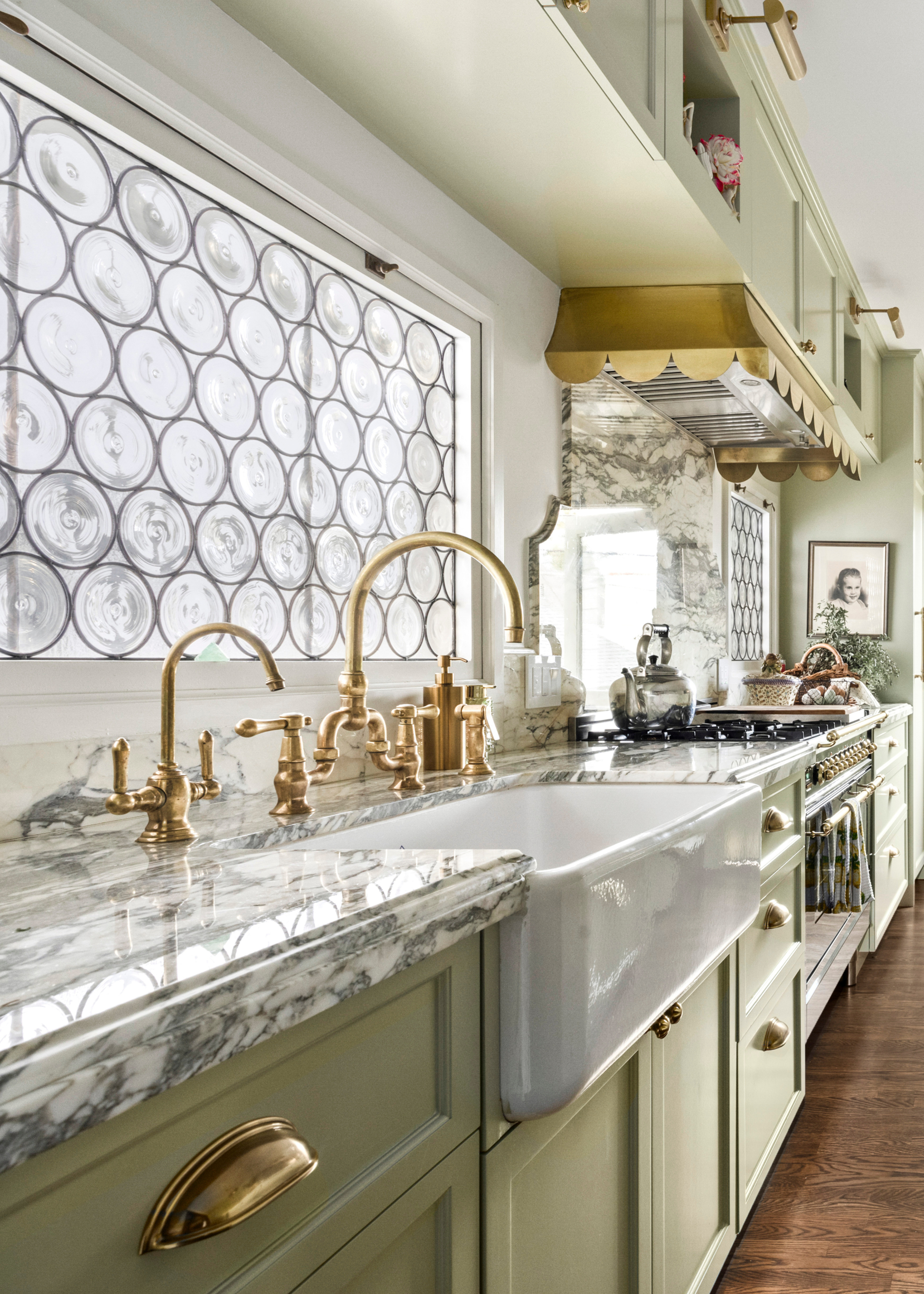 A green kitchen with stone counters, brass hardware and scalloped exhaust
