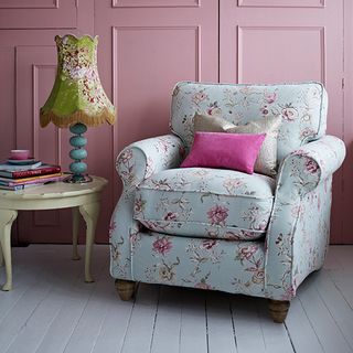 arm chair with pink wall and wooden floor and table with lamp and books