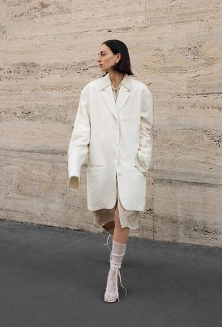 a woman's shirtdress outfit with a beige dress layered underneath a matching oversize blazer and matching sheer socks and thong sandals
