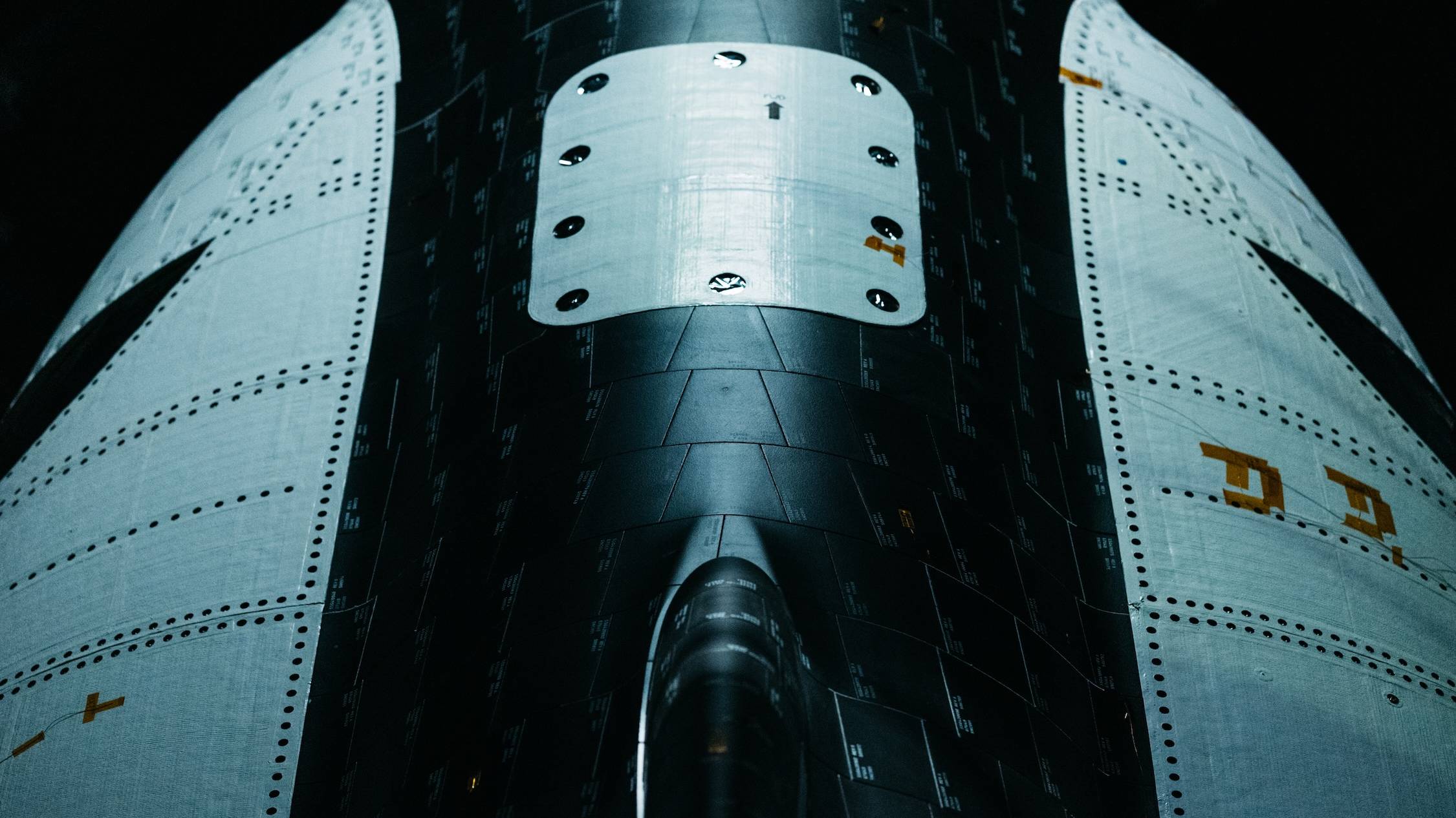 closeup view of a black and white space plane, showing black heat-shield tiles and white metal studded with rivets