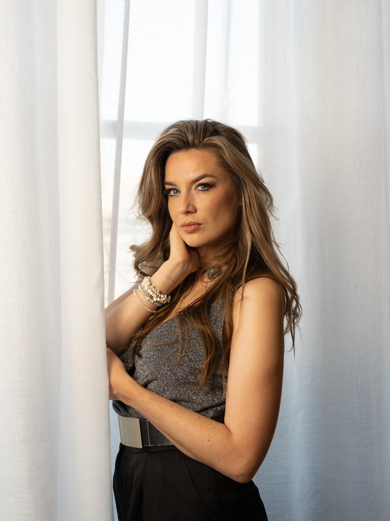Person posing in front of white drapes covering a window