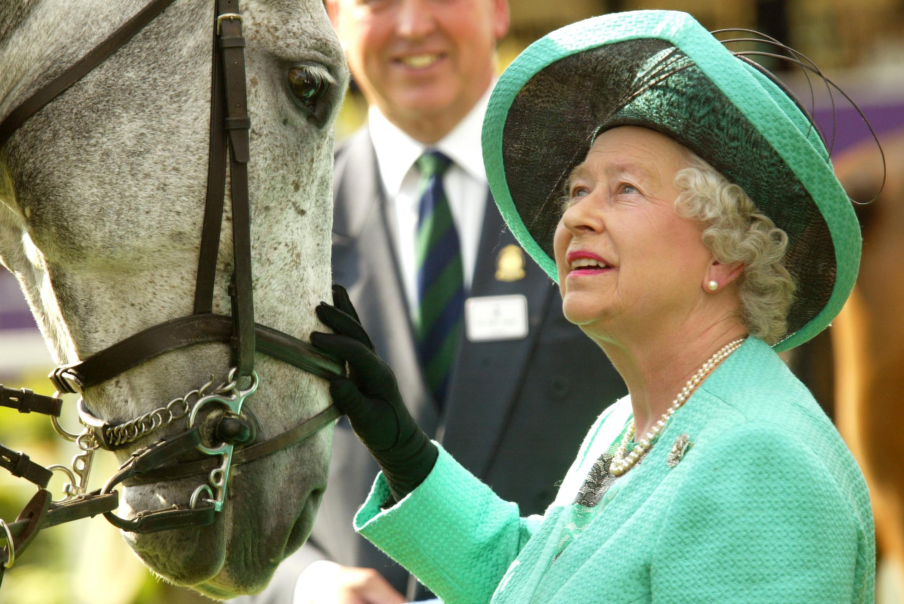 Queen Elizabeth wearing a green coat and hat petting a horse