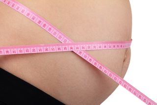 A pregnant woman's belly, with a measuring tape