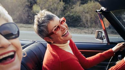 Two women laugh as they take a drive in a convertible.