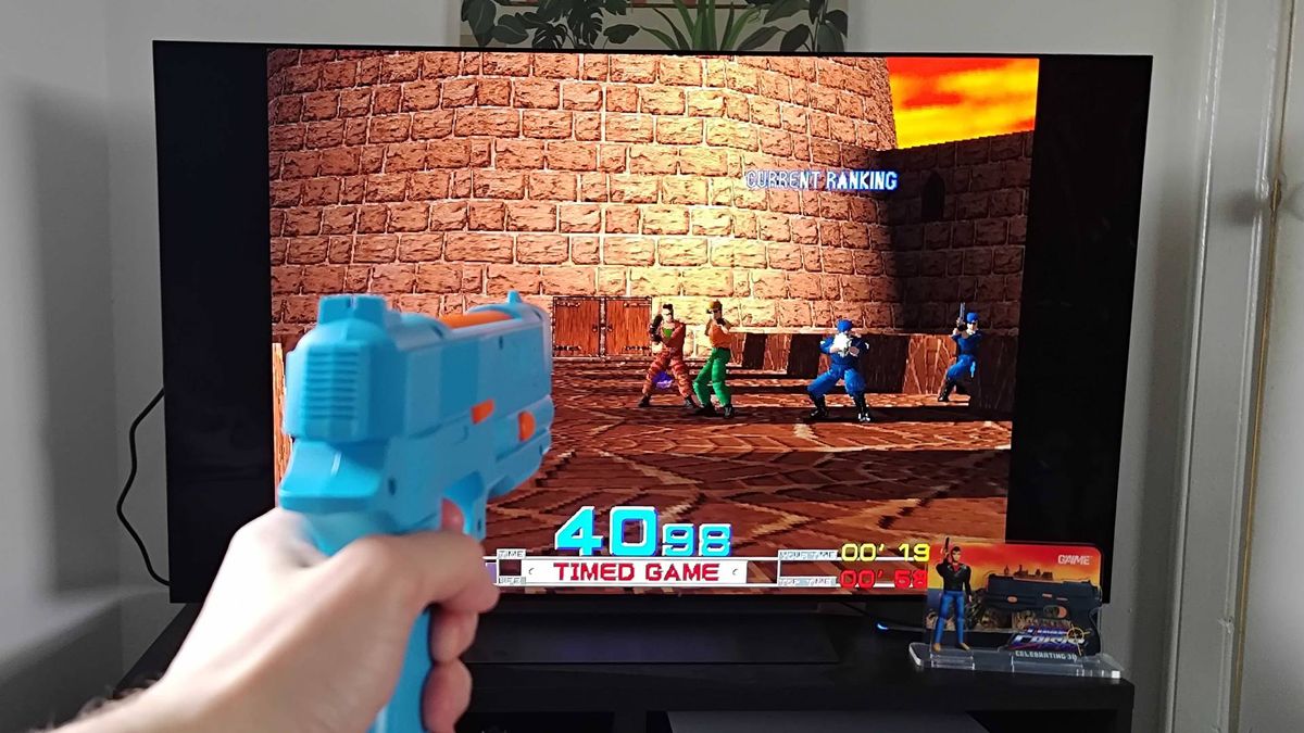 G'AIM'E console running Time Crisis on TV with hand using lightgun to shoot enemies.