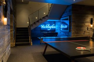 basement gaming room with table tennis, football table, artwork, wood cladding and neon sign, steps to upstairs, wall lights