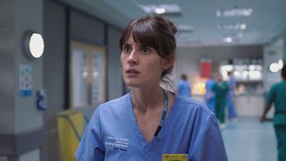 Jodie at work in blue scrubs looking very annoyed.