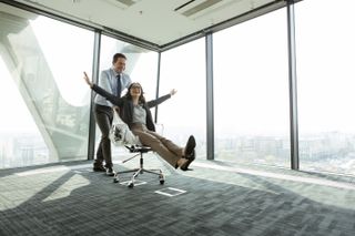 Businessman pushing businesswoman in office chair - stock photo