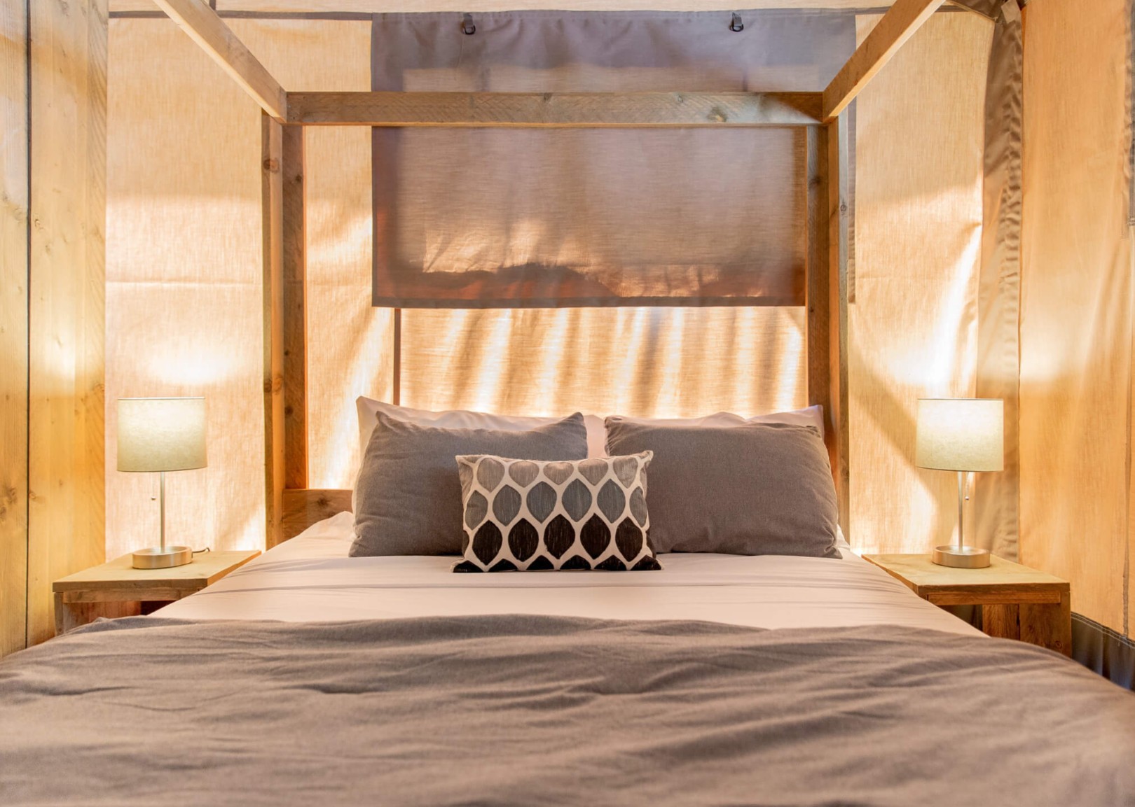 A comfortable-looking queen-size canopy bed at night in a glamping tent at Camp Little Arrow.
