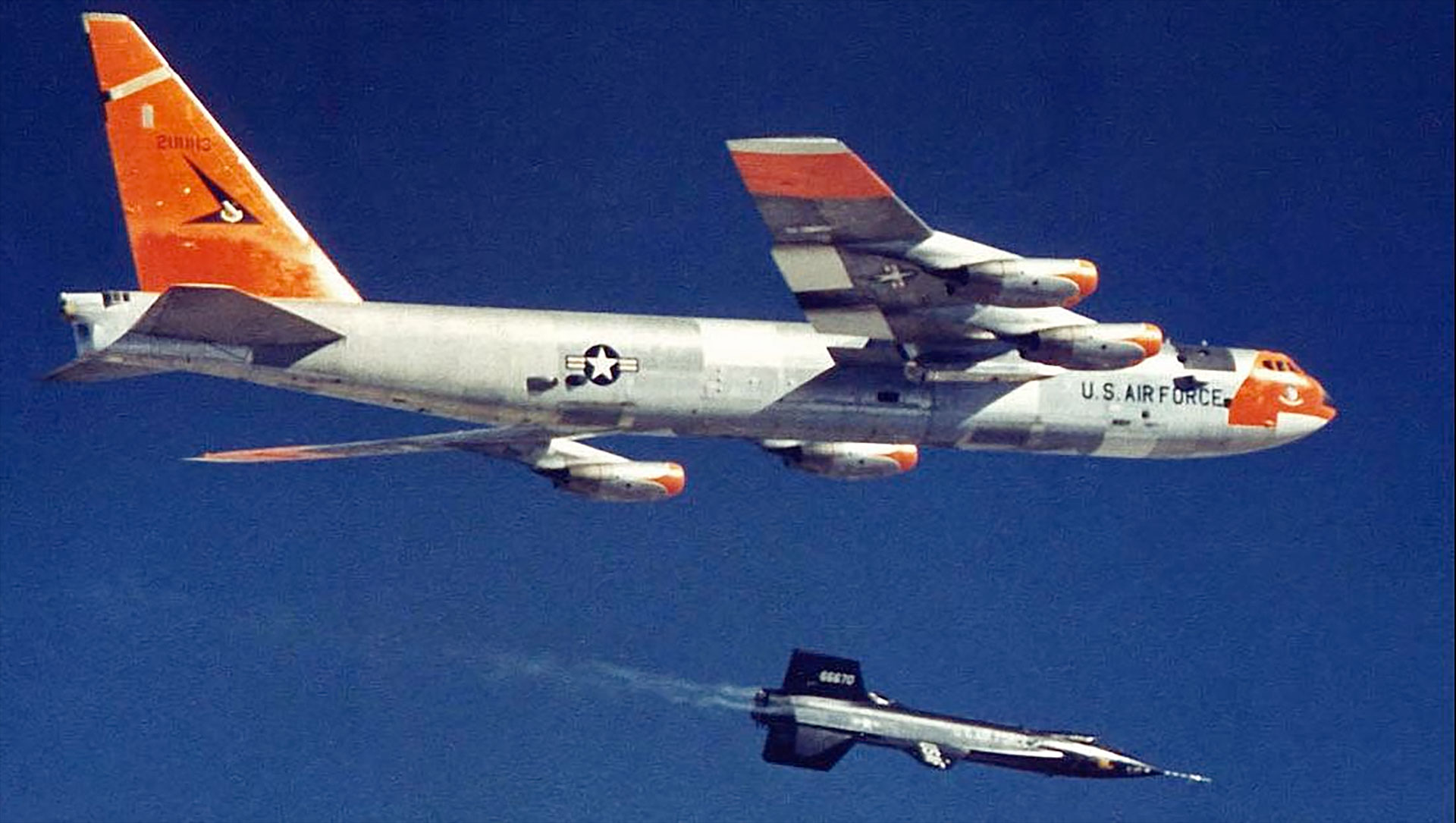 A small, sleek black rocket plane drops away from its much larger mothership aircraft at altitude