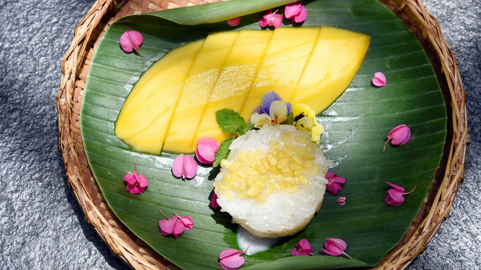 A wicker plate containing sliced mango and mound of sweet mango rice