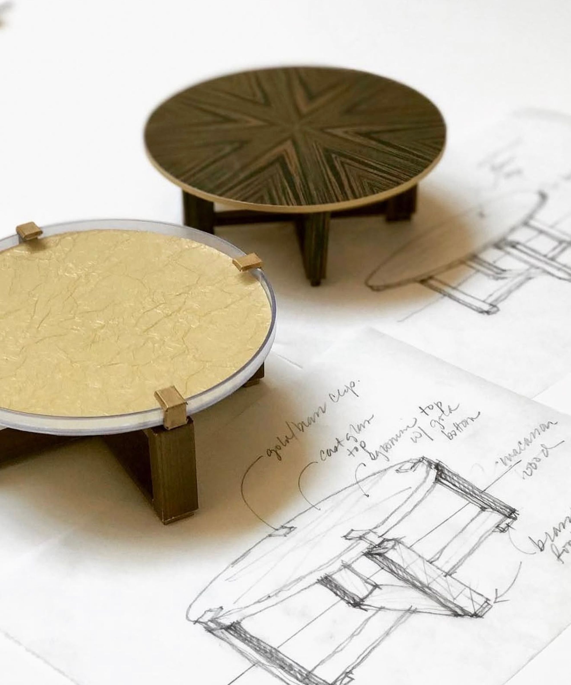 Close up of two mini models of round coffee tables, sat on top of black and white sketch of the models