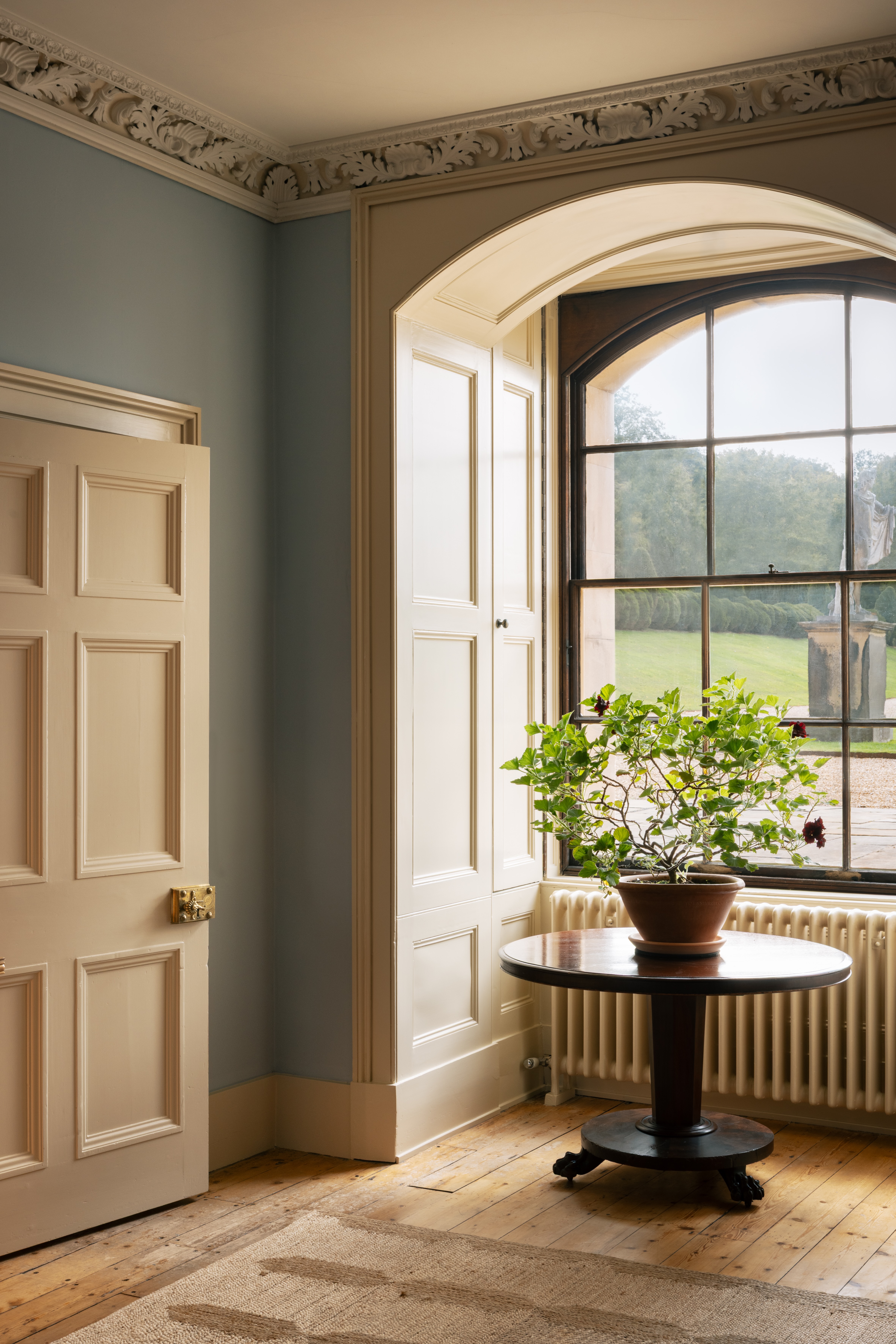 Corner of a double-heigh room with blue walls and white panelled doors and shutters