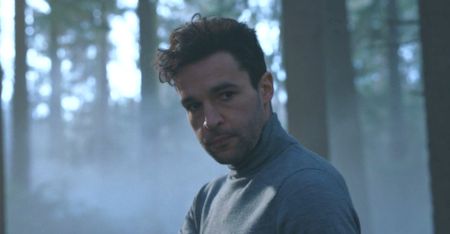 Christopher Abbott wearing a grey turtleneck in the woods during Kraven the Hunter. 