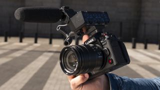Panasonic Lumix GH7 camera in hand with attached DMW-XLR2 microphone adapter