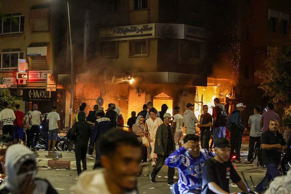 People pass by a bank building set on fire during a youth-led demonstration demanding reforms in the healthcare and education sectors in Sale on October 1, 2025.