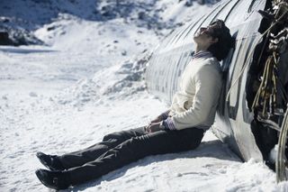 Enzo Vogrincic Roldán as a despondent Numa Turcatti sitting on a snowy mountaintop against the crashed remains of a commercial airplane in Society of the Snow