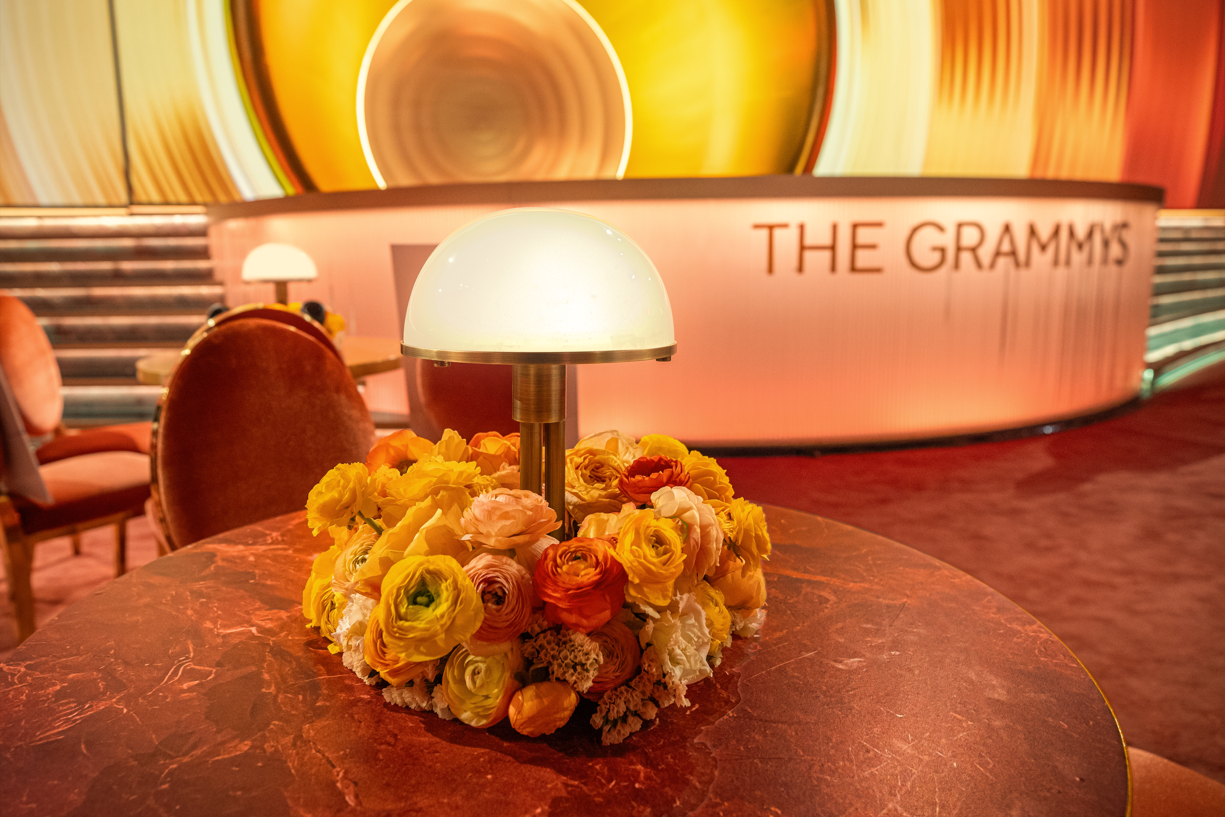 An aerial view of a performance stage with a sculptural, abstract structure of orange, red, and yellow swathes, foregrounded by a series of ceremony round tables with lamps as centerpieces.