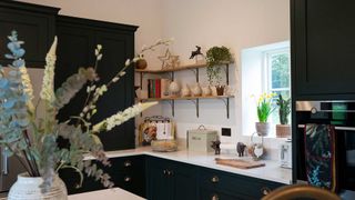 dark green kitchen with white worktops and open shelving