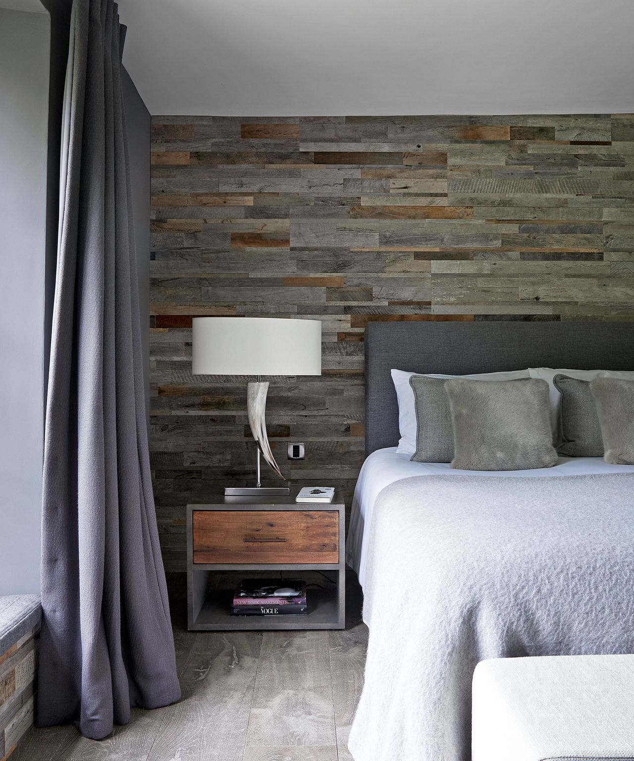 Neutral bedroom with reclaimed wood paneling on the walls, gray bed and gray curtains