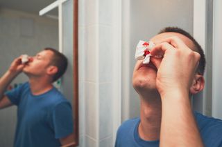A man holding a tissue to his bleeding nose in a restroom.