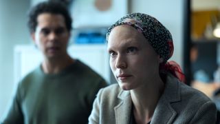 Tilda Cobham-Hervey as Lucy in a bright headscarf covering her hair loss while husband Justin looks on.