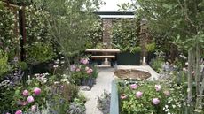 A modern garden with raised beds, seating area, and beds filled with flowers and shrubs