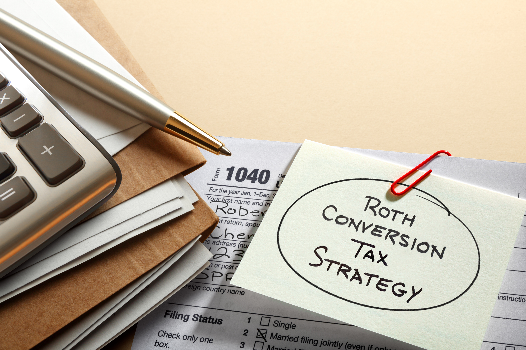 A note paper clipped to an IRS 1040 tax form with Roth IRA conversion tax strategy written on it rests next to a calculator.