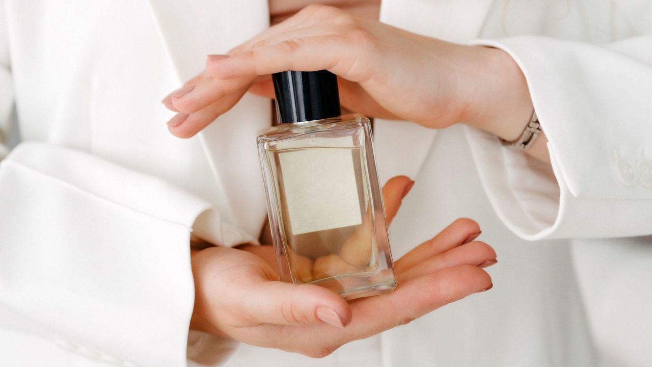 Woman in a white suit holding a perfume between her hands