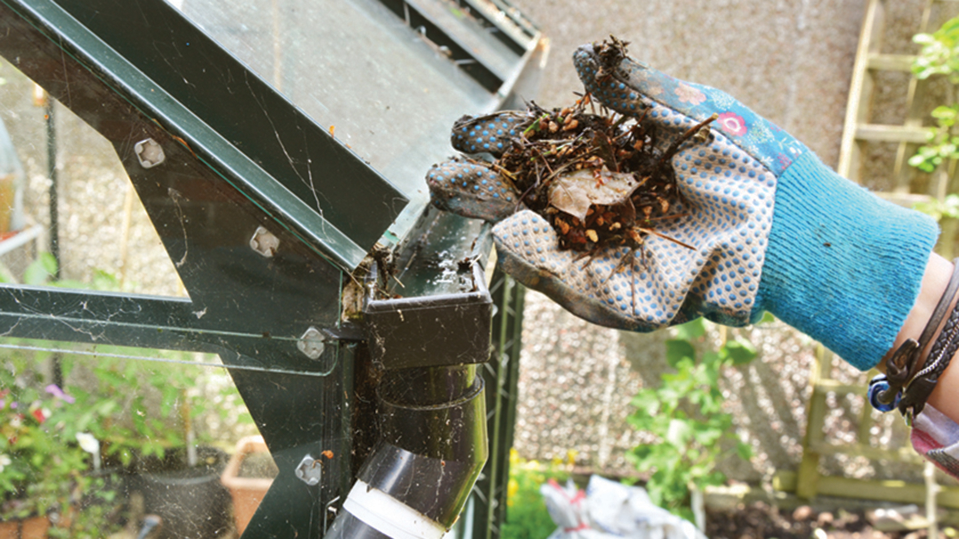 A gloved hand clearing debris from a gutter to show an essential home maintenance job to do before autumn