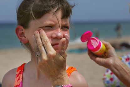 A woman puts sunscreen on a child's face.