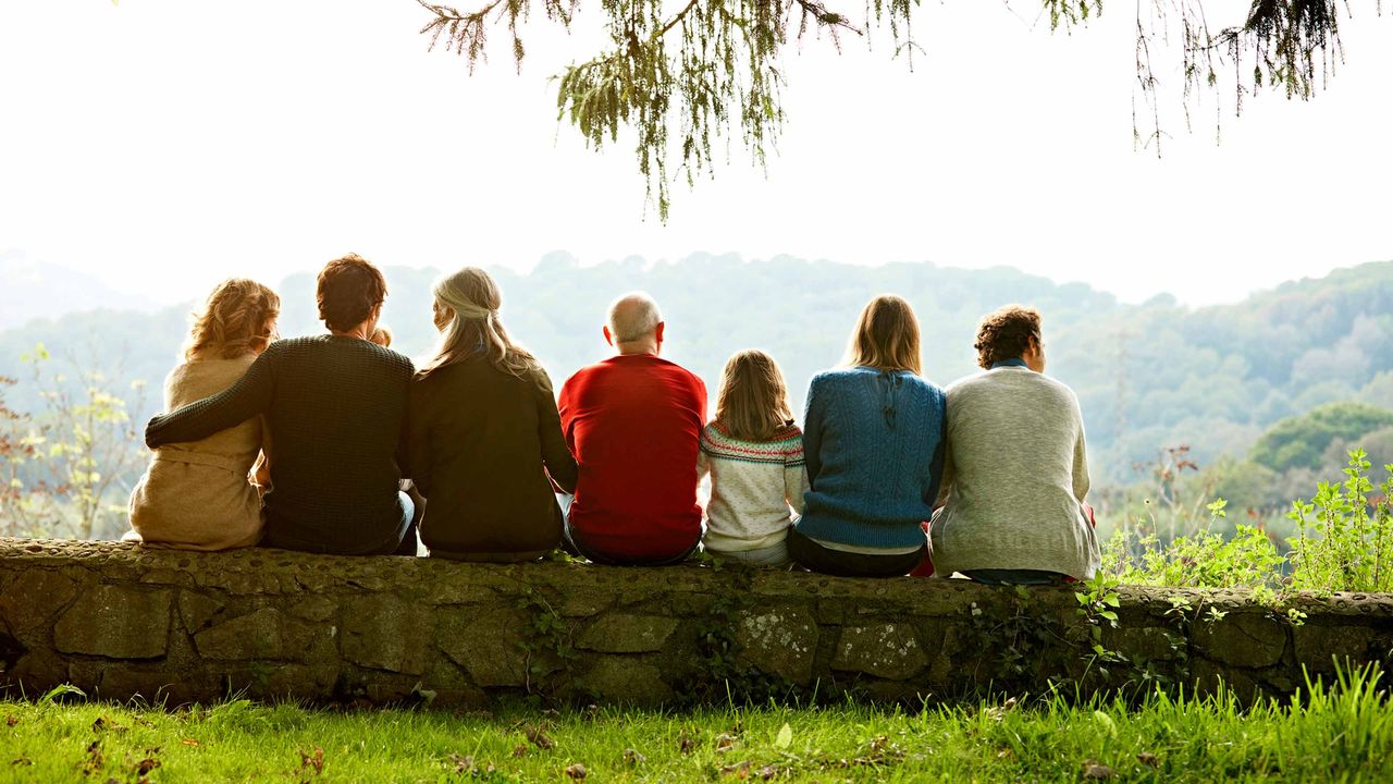 Multigeneration family relaxes on a retaining wall watching the sun set.