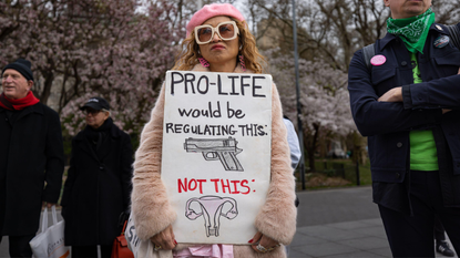 A woman holds a sign that reads: pro-life would be regulating guns, not this with a picture of a uterus