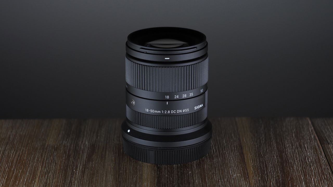 The Sigma 18-50mm f/2.8 DC DN | C Canon RF lens on a wooden surface against a dark background with moody lighting