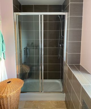 bathroom with dark tiles and small shower cubicle with wicker basket