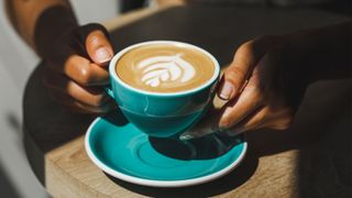 Woman's hands holding cappuccino coffee in cup with saucer