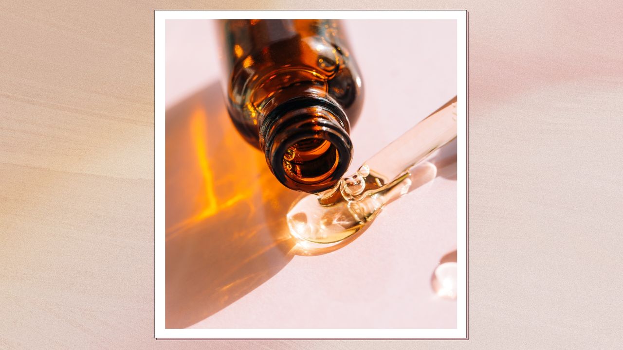 A close up of a brown serum bottle on it&#039;s side, spilling out a serum-like liquid, alongside a glass pipette and on a pink surface/ in a pink and orange gradient template