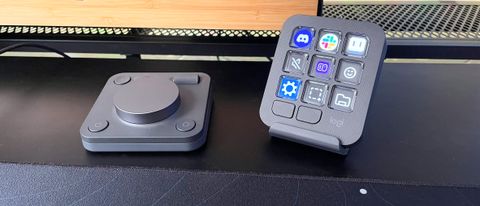 The Logitech MX Creative Console on a black desk in front of a wood monitor stand