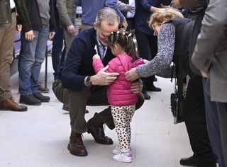 King Felipe crouching down to hug a young girl wearing a pink coat in a crowd