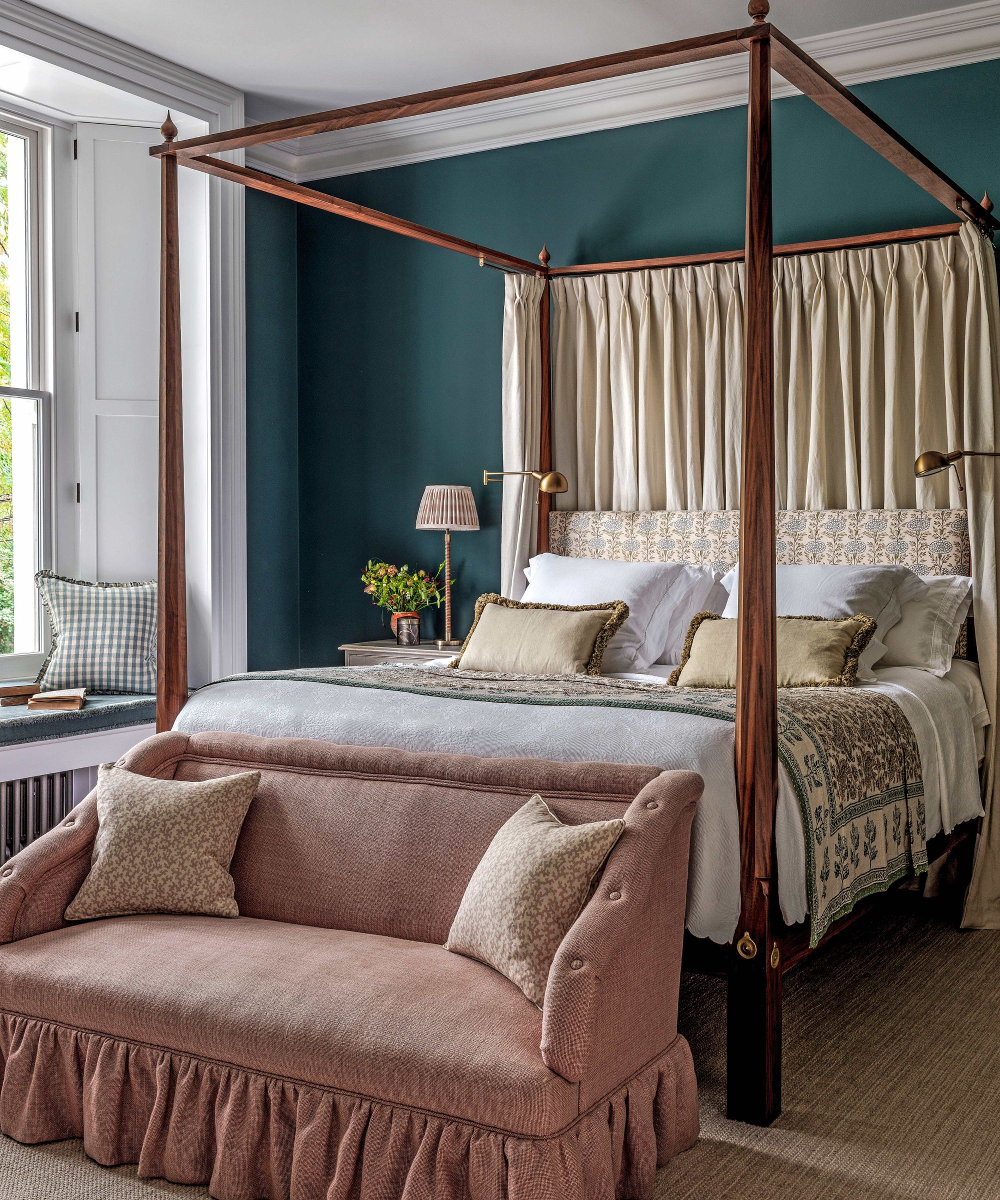 a dark green blue bedroom with a four poster bed, layered patterns and a pink ruffled foot of bed sofa