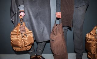 View of bottom half of two male models body's holding bags by Boss clothing.