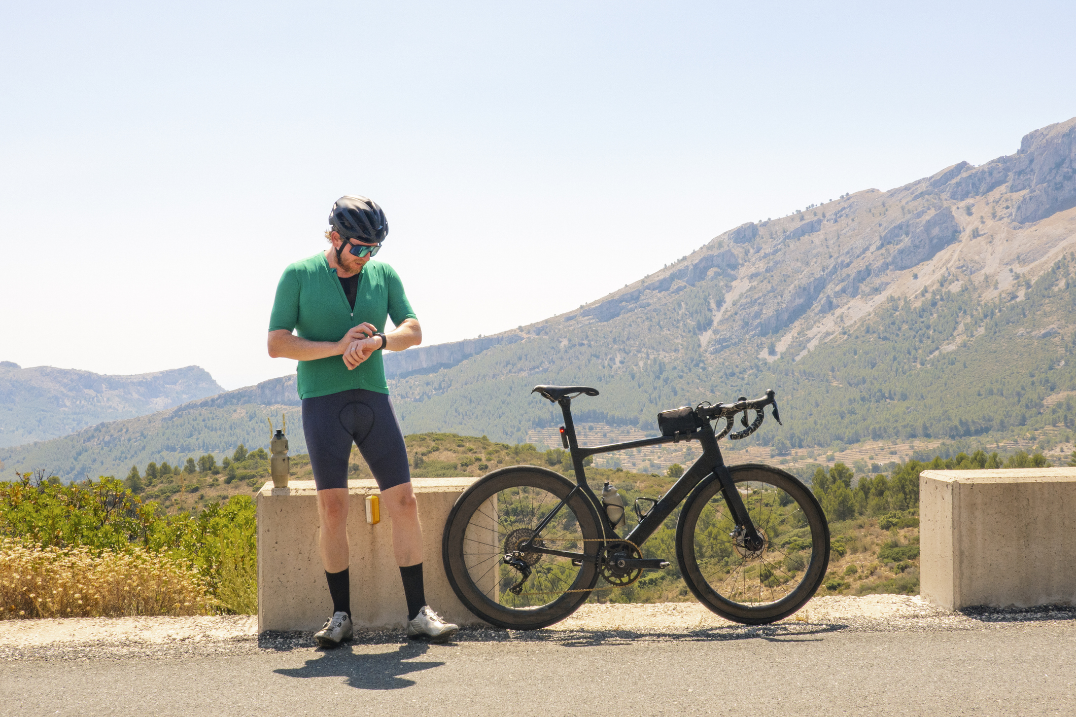 Ein Radfahrer steht neben seinem Fahrrad und schaut auf seine Smartwatch