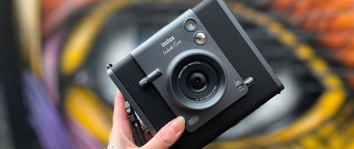 A hand holds the Fujifilm Instax Wide Evo 