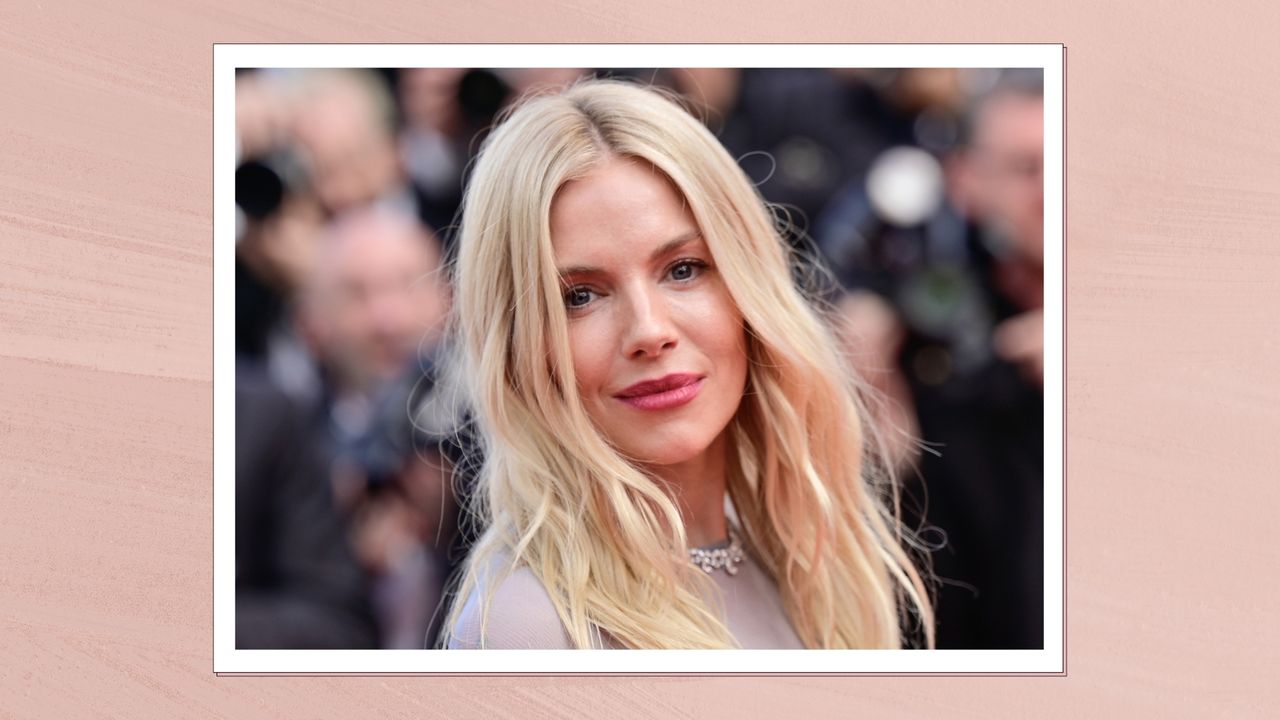 Sienna Milller is pictured with blonde wavy hair and a dark rosy lipstick look while attending the &quot;Horizon: An American Saga&quot; Red Carpet at the 77th annual Cannes Film Festival at Palais des Festivals on May 19, 2024 in Cannes, France in a pink template