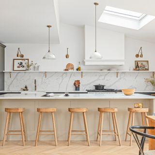 White kitchen with marble splashback and island with wooden bar stools