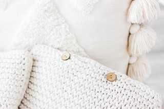 Soft, knitted cream and white cushions with knitted texture and tassels.