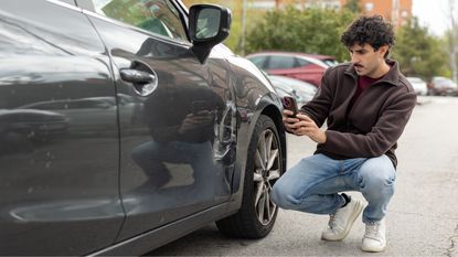 A young man photographs the damage to his car after a fender bender.