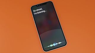 3D rendering of an iPhone showing the Siri &quot;Go ahead, I&#039;m listening&quot; message on an orange surface