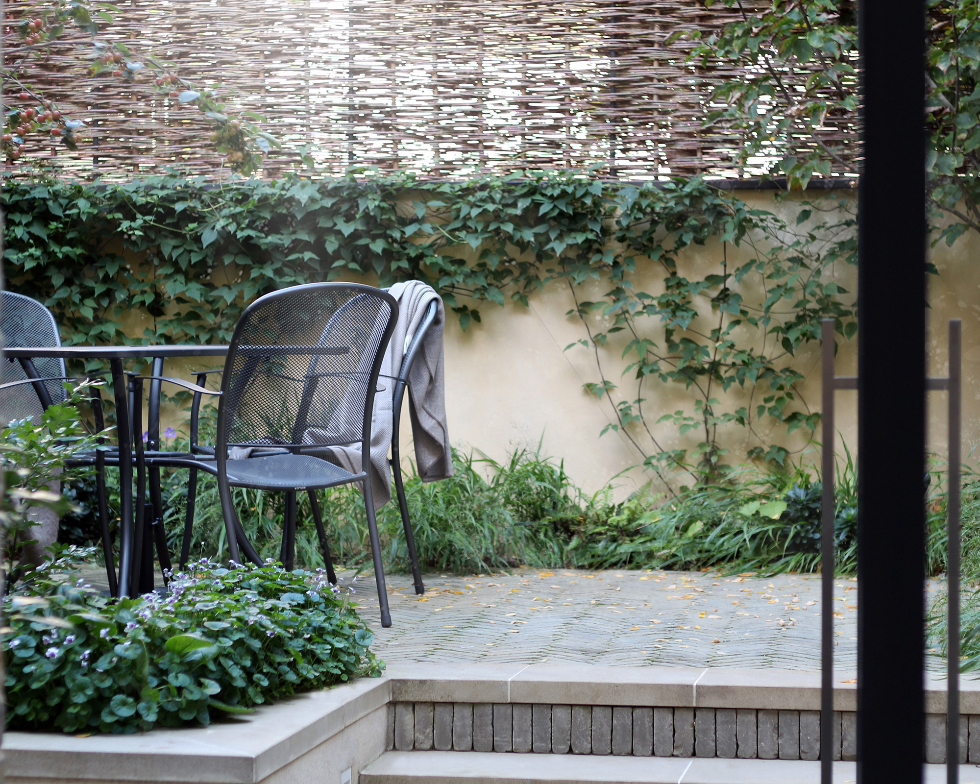 Close up of multi-level garden with black outdoor furniture, wall, climbers, wicker screen