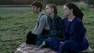 Ben Whishaw, Rooney Mara and Claire Foy in Women Talking. All three are sitting on a rug outside, looking into the distance